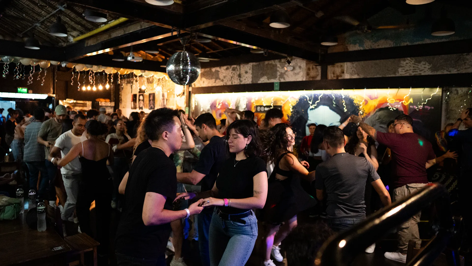 A packed dance social with a disco ball and dancers filling the floor